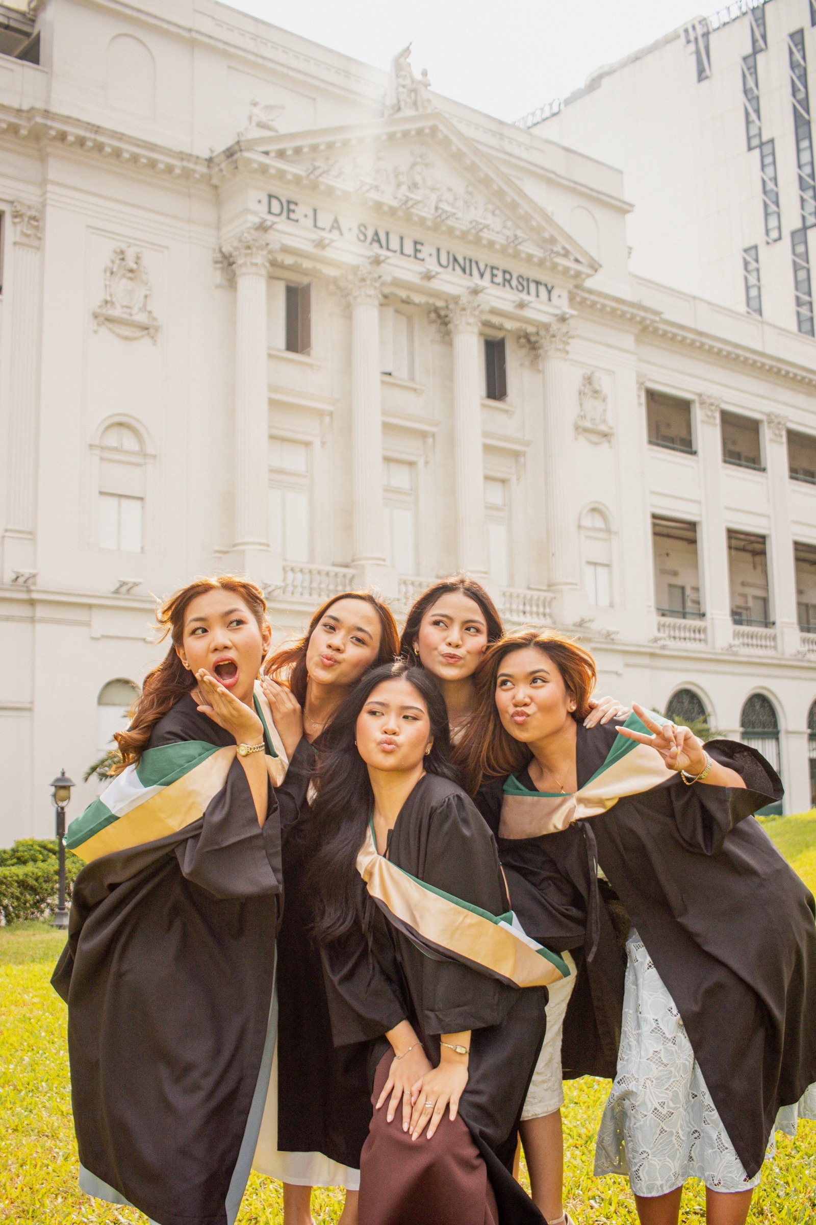 Six graduates lean into each other and laugh in front of the university facade