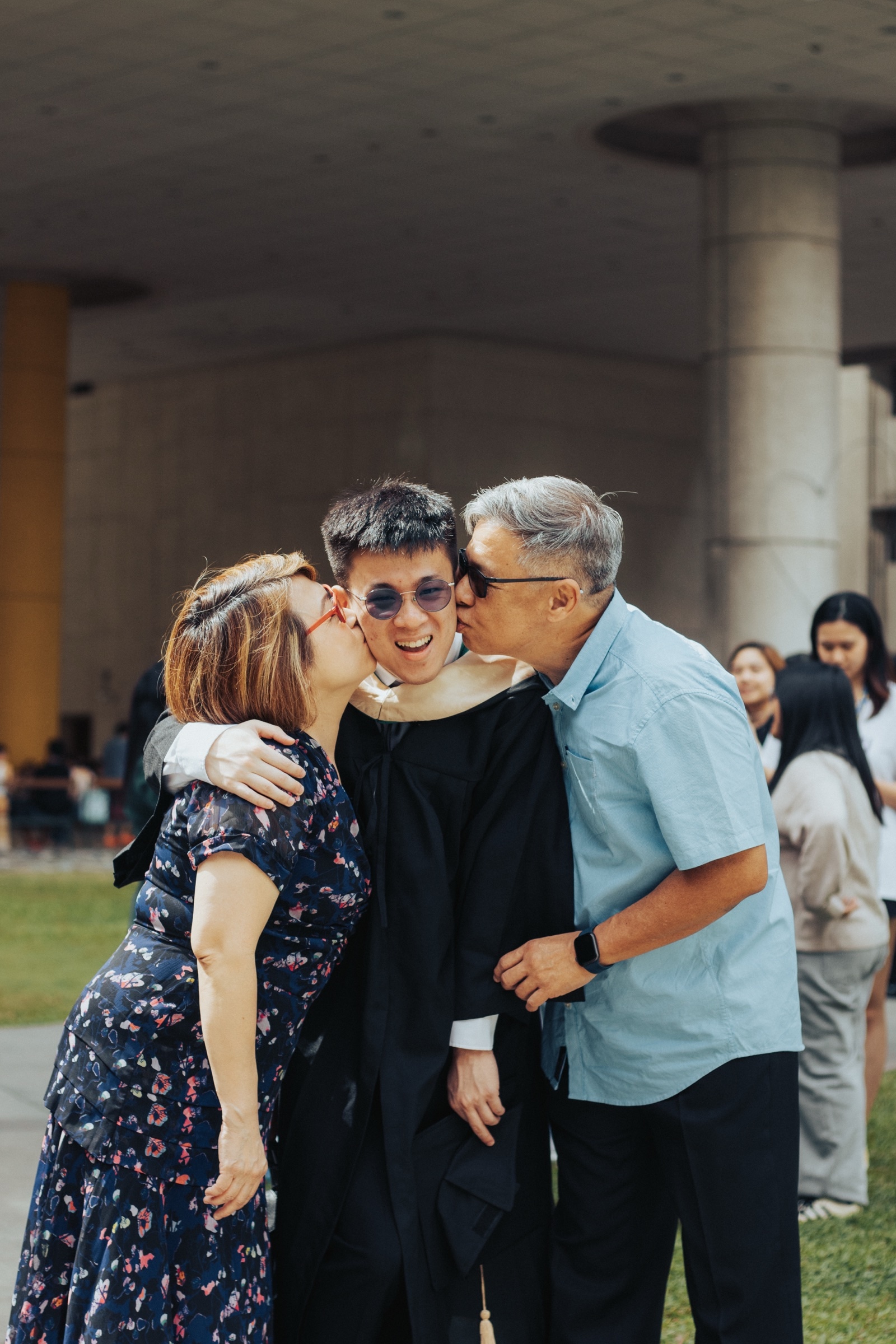 Two parents kiss a graduate on both cheeks outside the hall