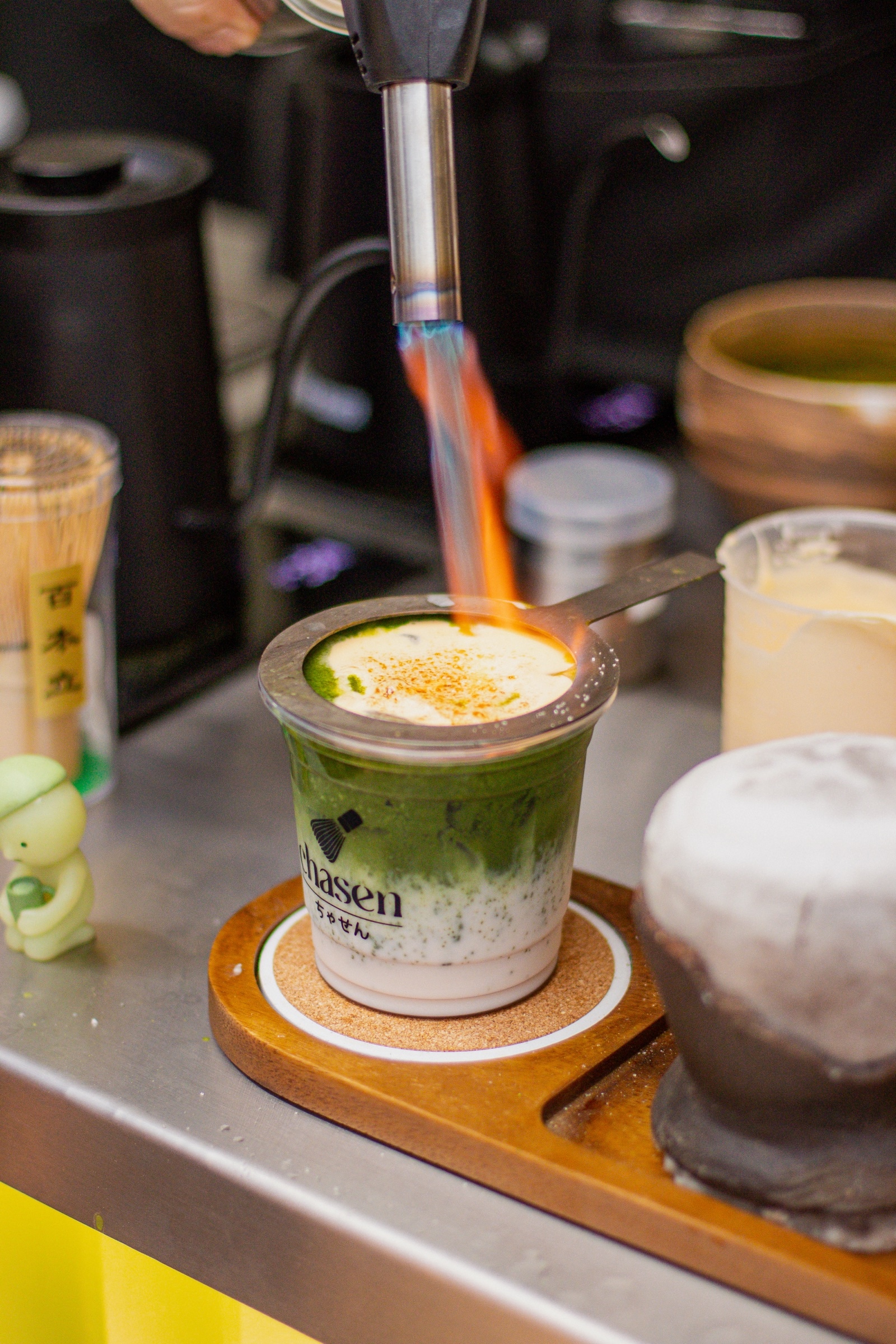A torch caramelises the top of a matcha drink at a market stall