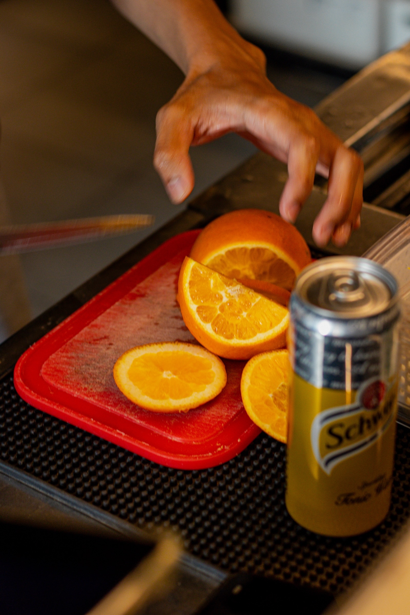 A hand arranges orange slices on a red tray beside a can of soda
